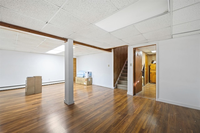 basement featuring dark hardwood / wood-style floors, a paneled ceiling, and baseboard heating