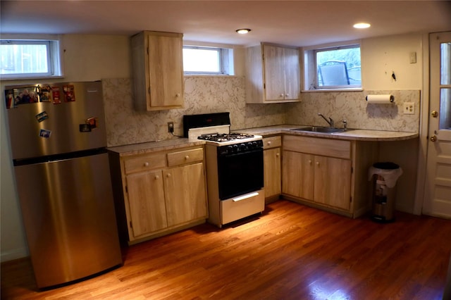 kitchen with freestanding refrigerator, light brown cabinetry, a sink, light countertops, and gas range