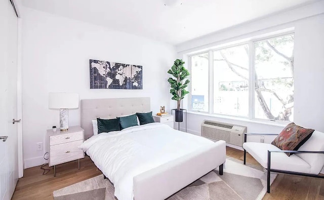 bedroom featuring multiple windows, an AC wall unit, and light hardwood / wood-style floors