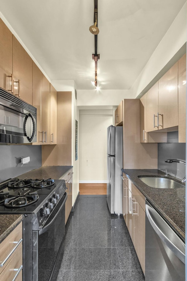 kitchen featuring stainless steel appliances, sink, dark stone countertops, and light brown cabinetry