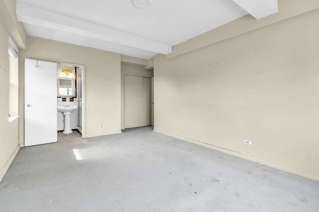 unfurnished bedroom featuring beamed ceiling, ensuite bath, sink, and a closet