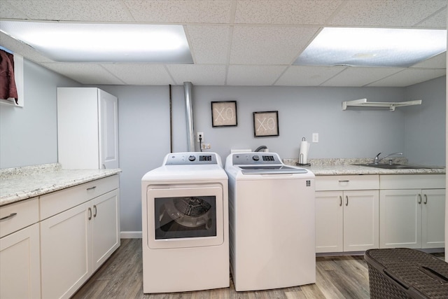 clothes washing area featuring sink, light hardwood / wood-style flooring, washing machine and dryer, and cabinets