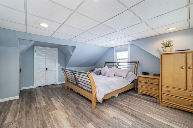 bedroom with a drop ceiling, hardwood / wood-style floors, and lofted ceiling