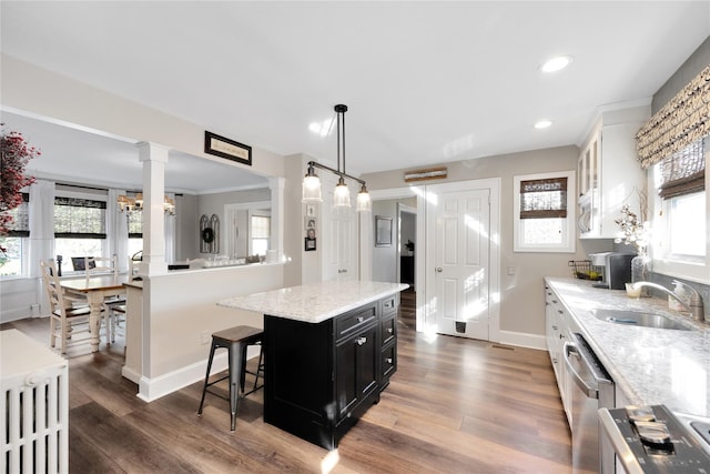 kitchen featuring decorative columns, sink, white cabinets, hanging light fixtures, and a center island