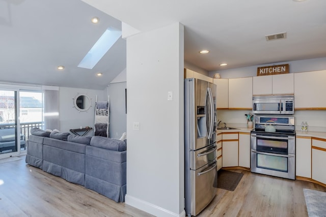 kitchen with vaulted ceiling with skylight, sink, stainless steel appliances, cream cabinets, and light hardwood / wood-style flooring