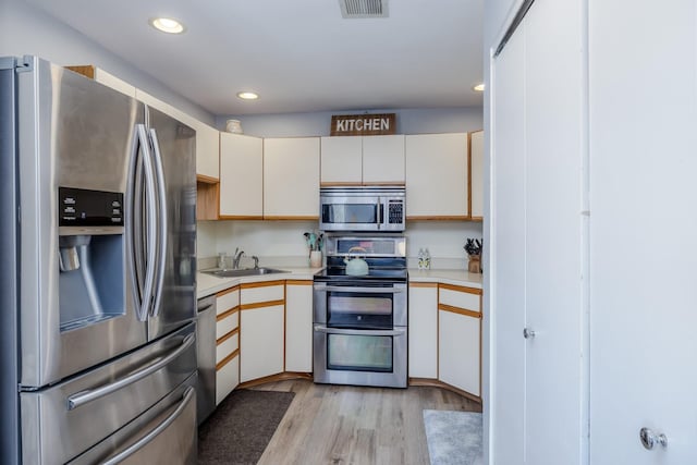 kitchen featuring stainless steel appliances, white cabinetry, sink, and light hardwood / wood-style flooring