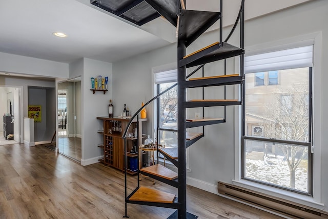 stairway featuring hardwood / wood-style flooring, a healthy amount of sunlight, and a baseboard heating unit