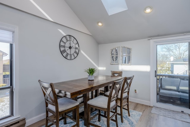 dining space featuring vaulted ceiling with skylight and light hardwood / wood-style flooring