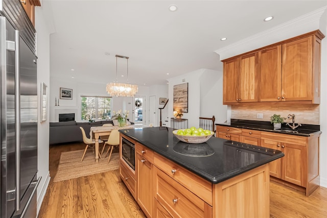 kitchen with sink, light hardwood / wood-style flooring, hanging light fixtures, built in appliances, and a kitchen island