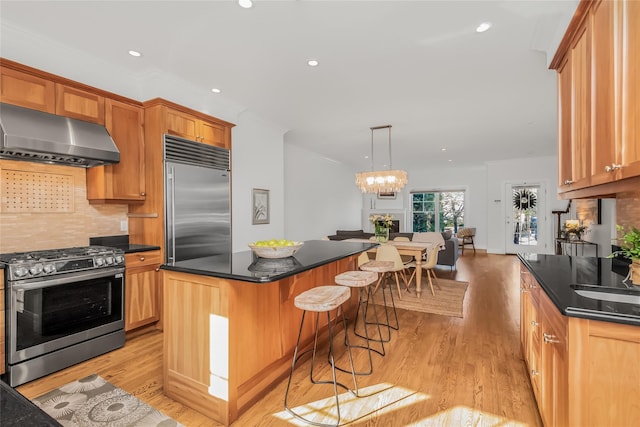 kitchen with pendant lighting, appliances with stainless steel finishes, a center island, tasteful backsplash, and wall chimney exhaust hood