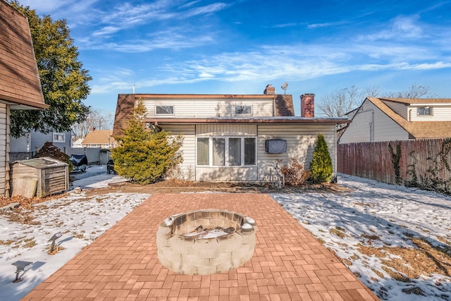 snow covered back of property with an outdoor fire pit and a patio