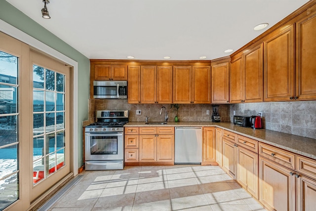 kitchen featuring sink, dark stone countertops, backsplash, light tile patterned floors, and stainless steel appliances