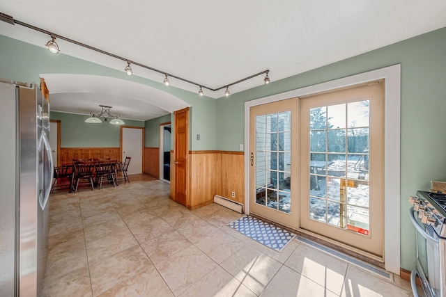 doorway with a baseboard heating unit, light tile patterned floors, and wood walls