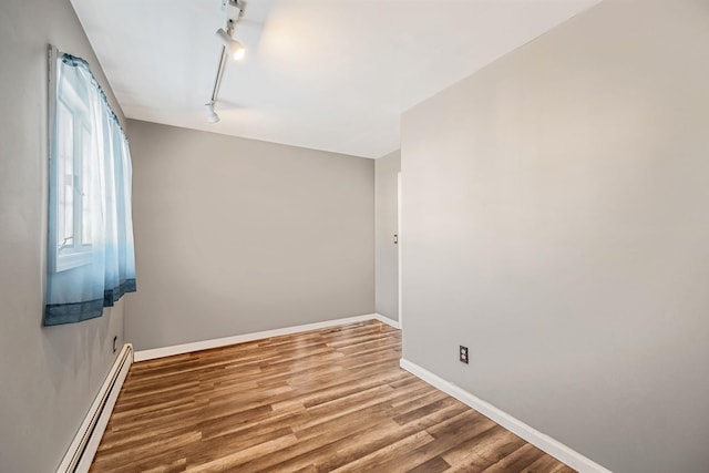 spare room featuring baseboard heating, track lighting, and hardwood / wood-style flooring