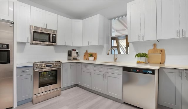 kitchen with tasteful backsplash, appliances with stainless steel finishes, sink, and gray cabinetry