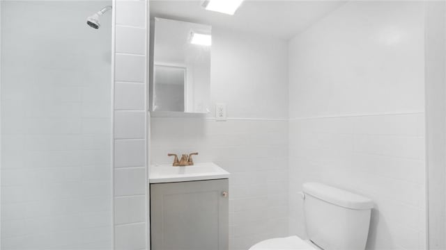 bathroom featuring toilet, a tile shower, tile walls, and vanity