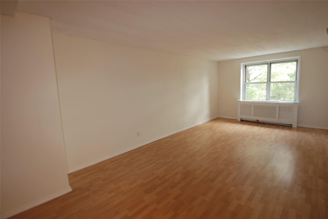 unfurnished room with radiator and light wood-type flooring