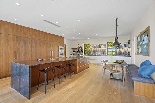 kitchen featuring a breakfast bar, decorative light fixtures, light wood-type flooring, a large island, and decorative backsplash