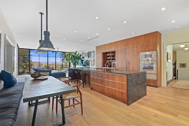 kitchen featuring stainless steel double oven, decorative light fixtures, a wall of windows, and light hardwood / wood-style flooring