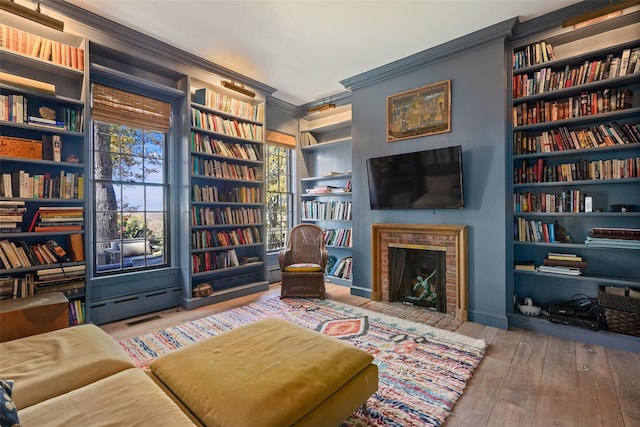 sitting room with crown molding, a fireplace, built in shelves, and wood-type flooring