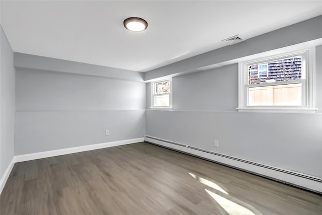 spare room featuring baseboard heating and dark hardwood / wood-style flooring