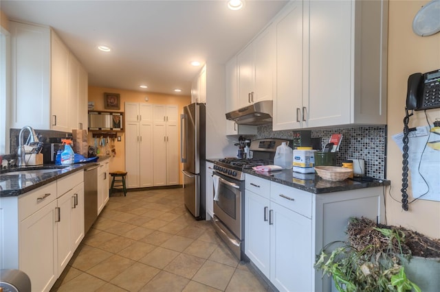 kitchen with stainless steel appliances, white cabinetry, sink, and dark stone countertops