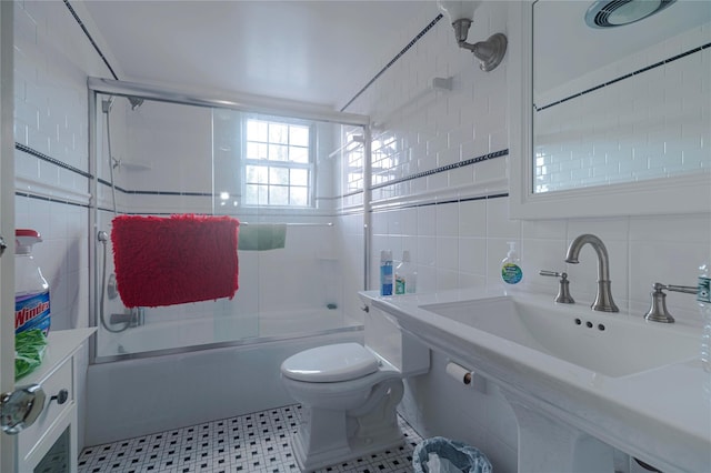 full bathroom with tile walls, sink, shower / bath combination with glass door, and toilet