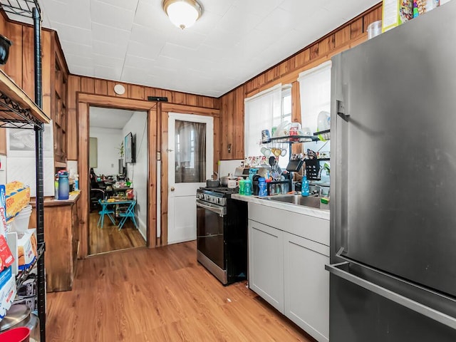 kitchen with sink, appliances with stainless steel finishes, wood walls, white cabinets, and light wood-type flooring