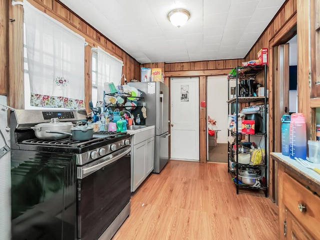 kitchen with light wood-type flooring, stainless steel range with gas stovetop, and wooden walls