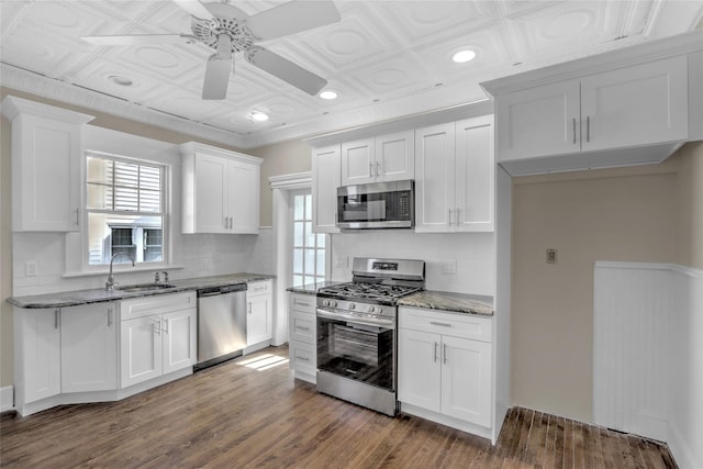 kitchen with appliances with stainless steel finishes, hardwood / wood-style floors, white cabinetry, sink, and dark stone counters