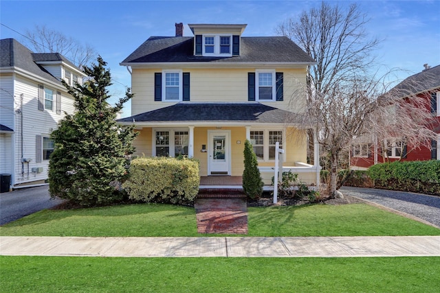 american foursquare style home with cooling unit, a chimney, a porch, and a front lawn