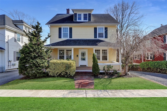 traditional style home with a chimney, roof with shingles, a porch, and a front lawn