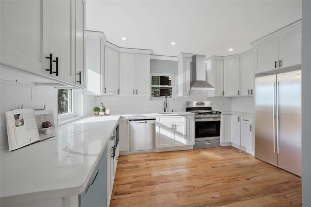 kitchen with sink, wall chimney range hood, stainless steel appliances, light stone countertops, and white cabinets