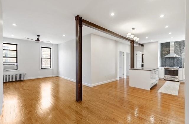 unfurnished living room featuring radiator, ceiling fan with notable chandelier, and light hardwood / wood-style floors