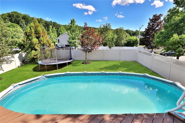 view of swimming pool with a trampoline, a fenced backyard, a yard, and a deck