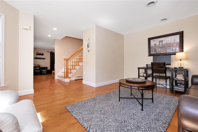 living area with stairway, baseboards, a baseboard heating unit, and wood finished floors