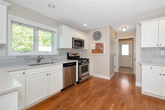 kitchen featuring appliances with stainless steel finishes, light countertops, light wood-style floors, white cabinetry, and a sink