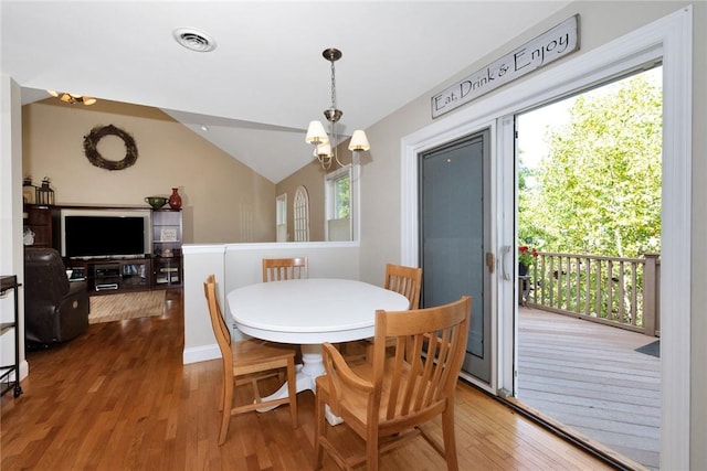 dining area with a chandelier, visible vents, vaulted ceiling, and wood finished floors