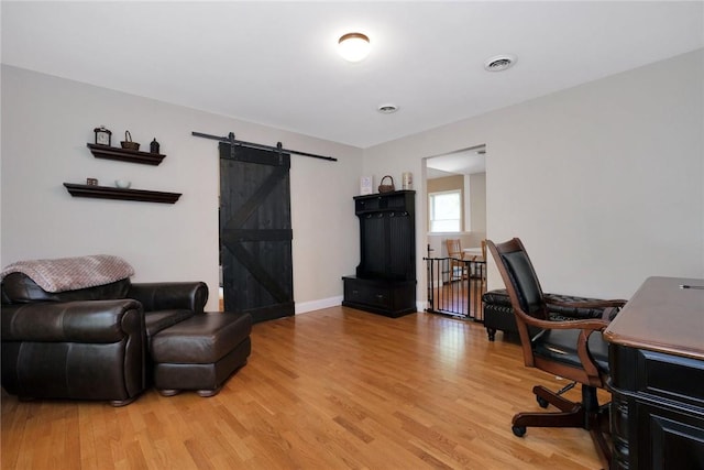 home office featuring light wood-style floors, visible vents, baseboards, and a barn door