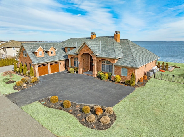 view of front of house featuring brick siding, aphalt driveway, a water view, fence, and a front yard