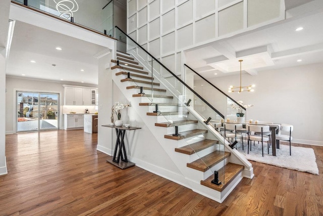 staircase with an inviting chandelier, wood-type flooring, coffered ceiling, and a high ceiling