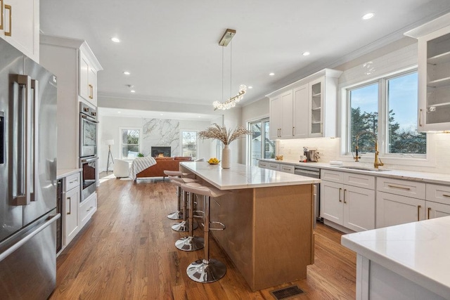 kitchen featuring sink, appliances with stainless steel finishes, a center island, white cabinets, and decorative light fixtures