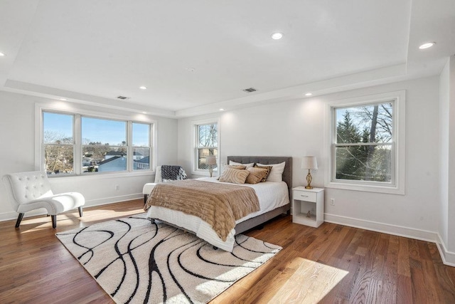 bedroom with wood-type flooring, a water view, and a tray ceiling