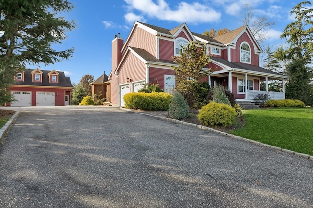 view of front facade featuring a porch, aphalt driveway, a garage, a chimney, and a front yard