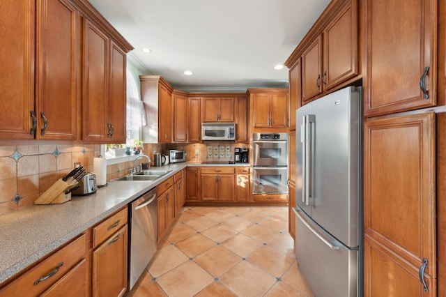 kitchen featuring light tile patterned floors, a sink, appliances with stainless steel finishes, backsplash, and brown cabinets