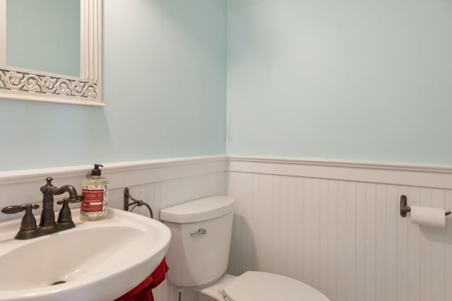 half bath featuring toilet, a sink, and wainscoting