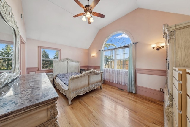 bedroom featuring lofted ceiling, a wainscoted wall, multiple windows, and light wood finished floors