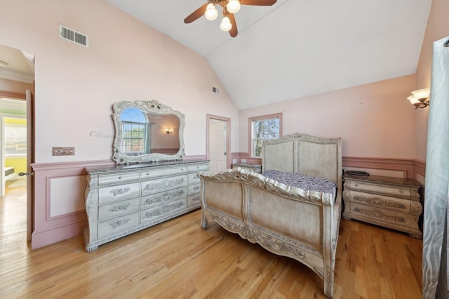 bedroom with a wainscoted wall, visible vents, vaulted ceiling, and wood finished floors