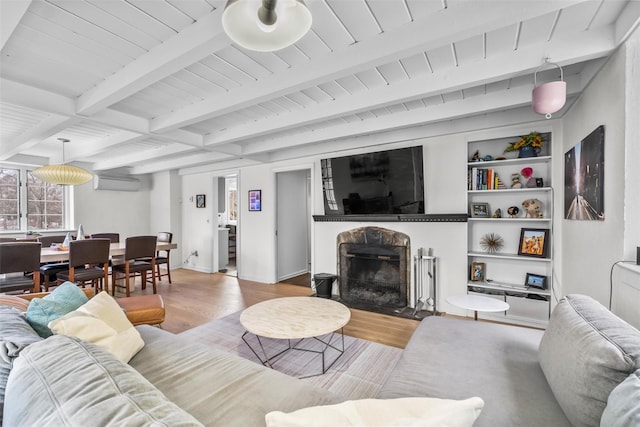 living area with a fireplace with flush hearth, wood ceiling, a wall mounted AC, beam ceiling, and light wood finished floors