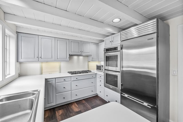 kitchen with dark wood-style flooring, light countertops, a sink, built in appliances, and beamed ceiling